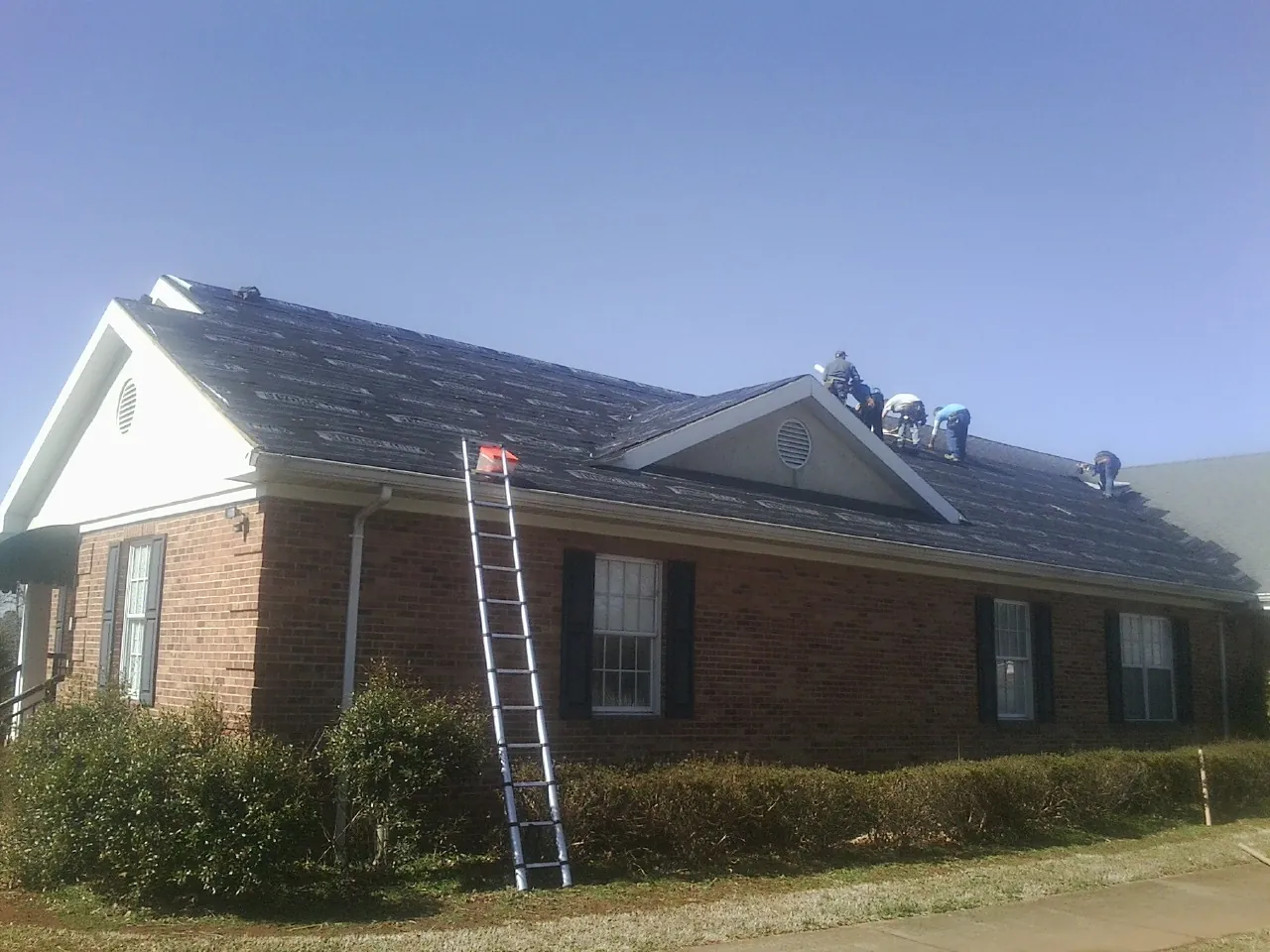 Crew tearing shingles off a brick ranch roof with a ladder set — Emergency Roof Repair work by our crew in Changewater