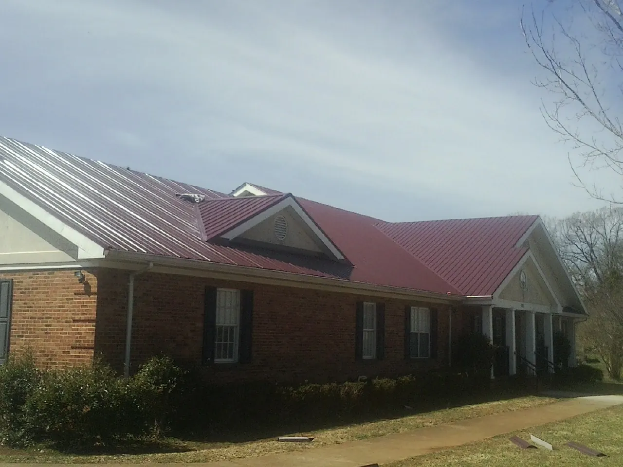 Red metal roof with gabled entries on a long brick building, from a Hail Damage Roof Repair job in Changewater