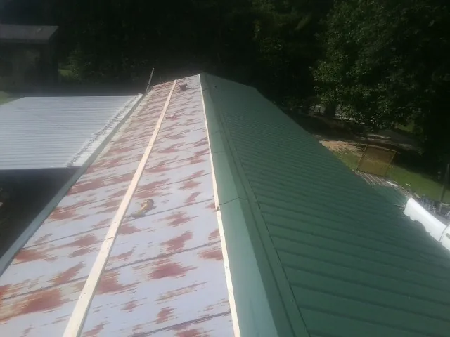 Old rusted panels beside newly installed green metal roofing — Wind Damage Roof Repair by Roofing Brothers in Changewater