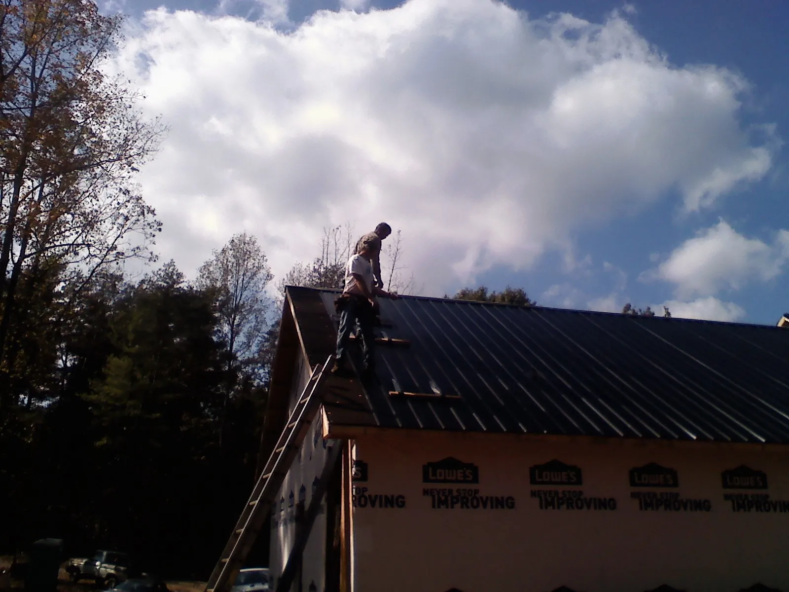 Roofer fastening dark metal panels high against a cloudy sky, from a Roof Inspection job in Changewater