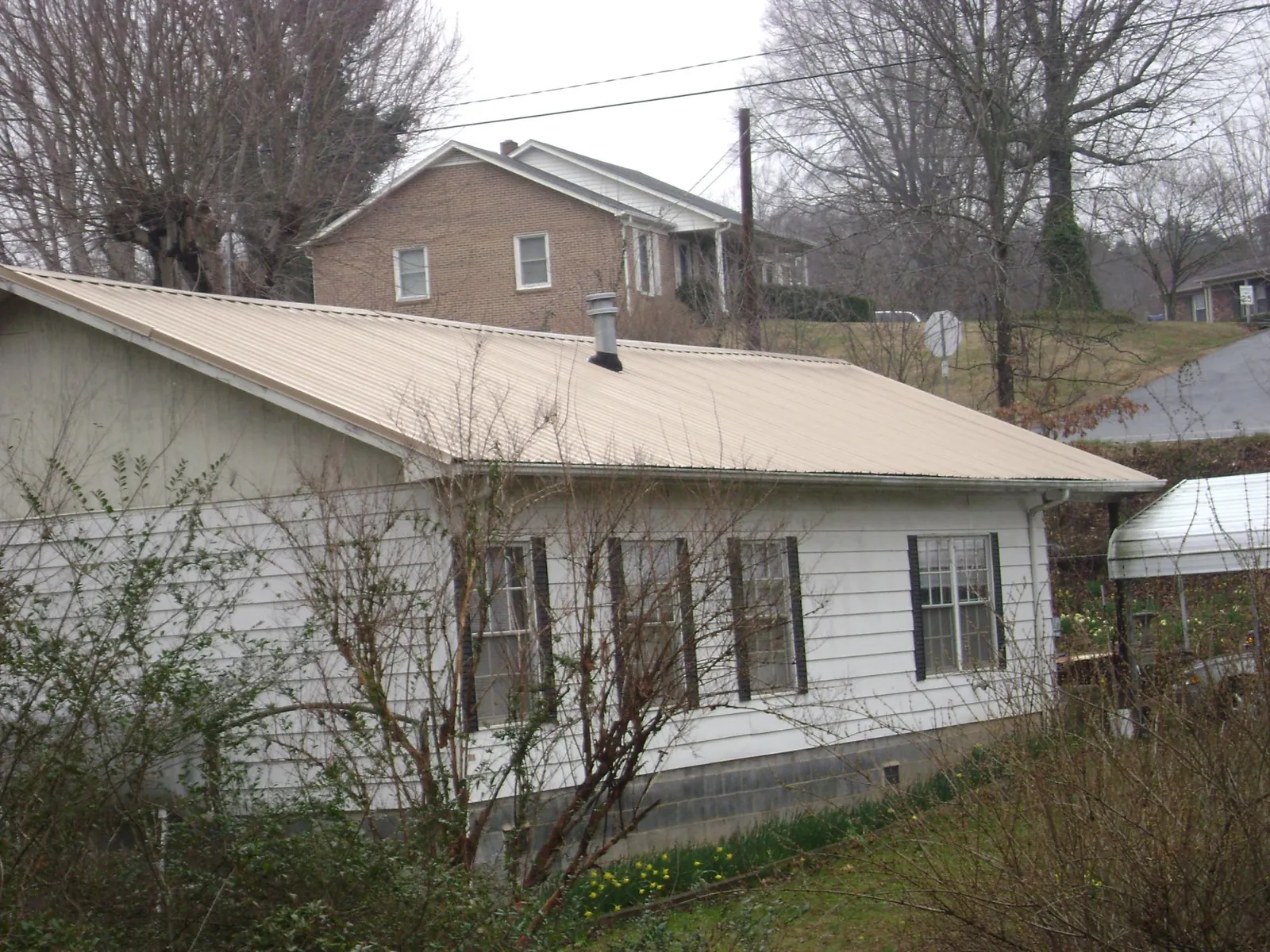 Tan metal roof on a white sided house set into a hillside in Changewater